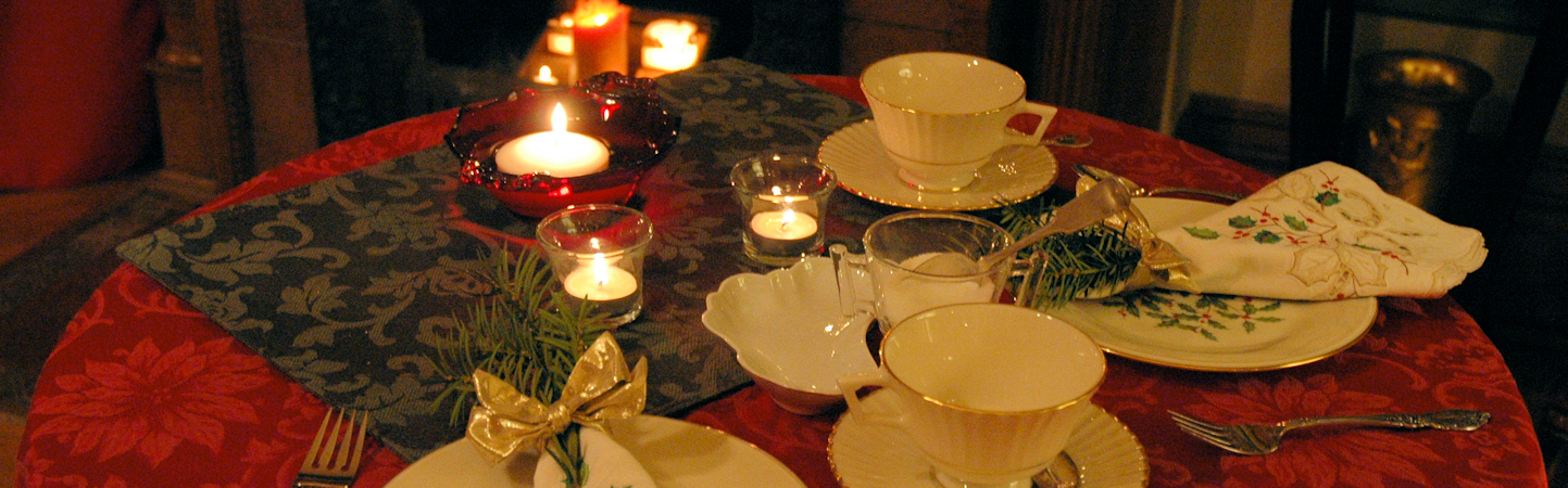 Table for two set for Christmas Tea with red damask cloth, linens embroidered in green and red, creamy Lennox China, silver, candles, and fresh greenery.